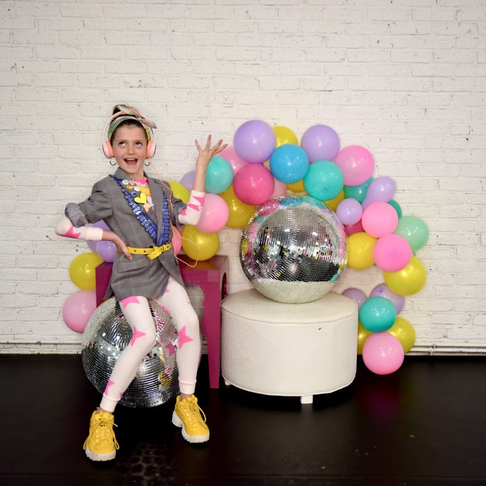 Fun image of dancer posing in front of a colorful balloon garland and disco balls!