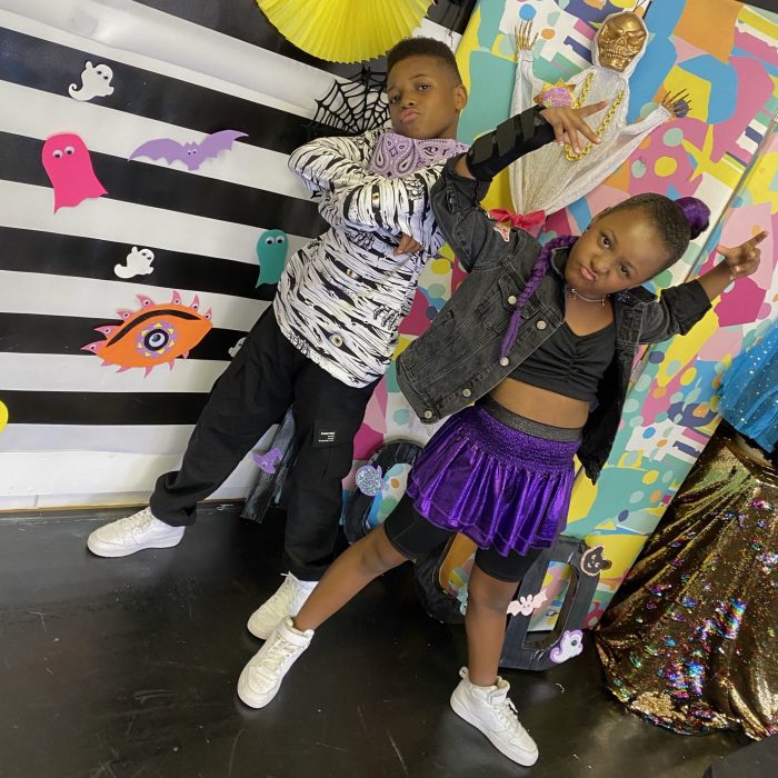 Two young black dancers in a fun pose in front of a Halloween background. 