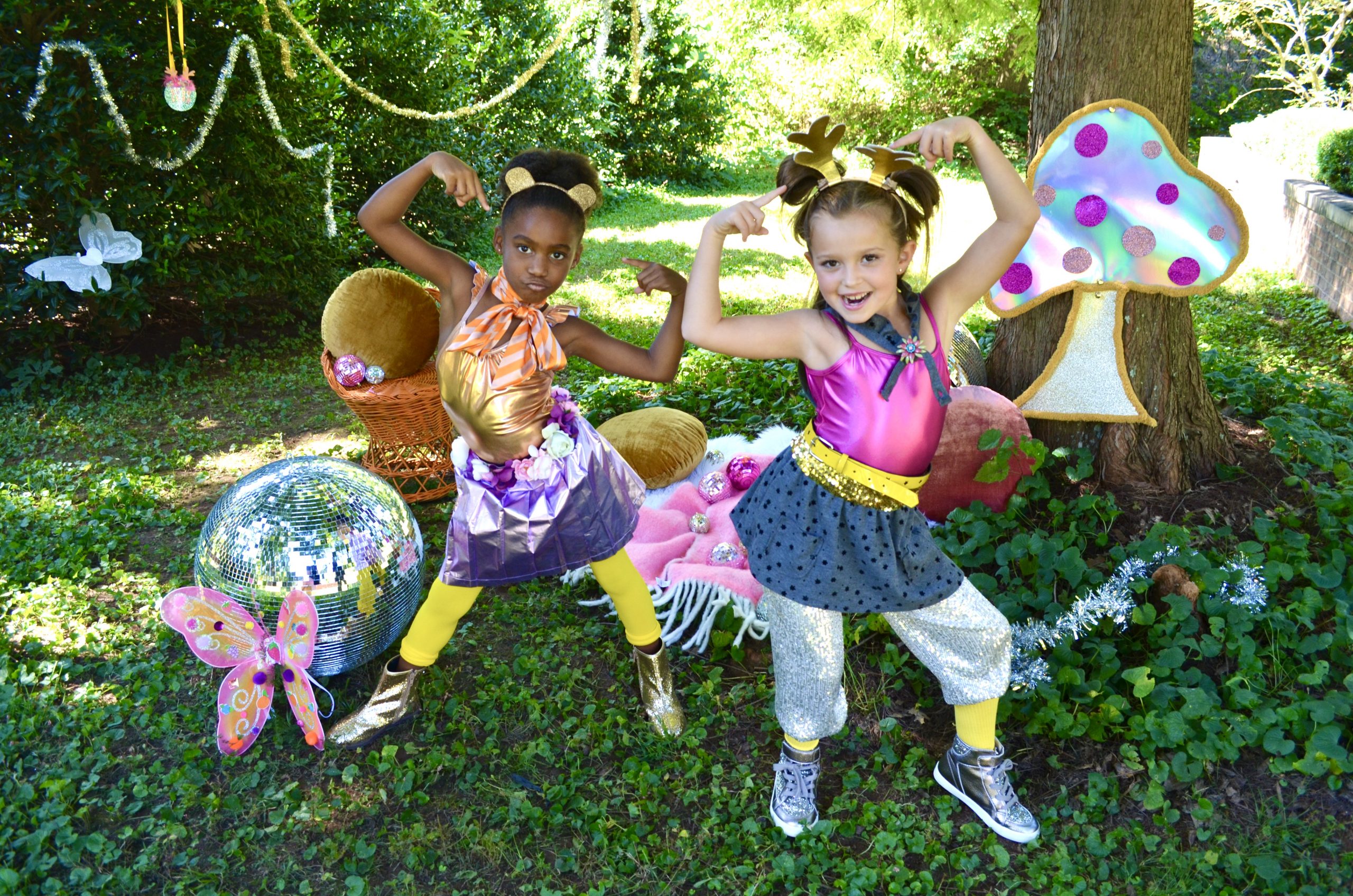 Two young dancers posing in a woodlands scene with disco balls and a sparkly mushroom, getting ready for a fun dance activity!