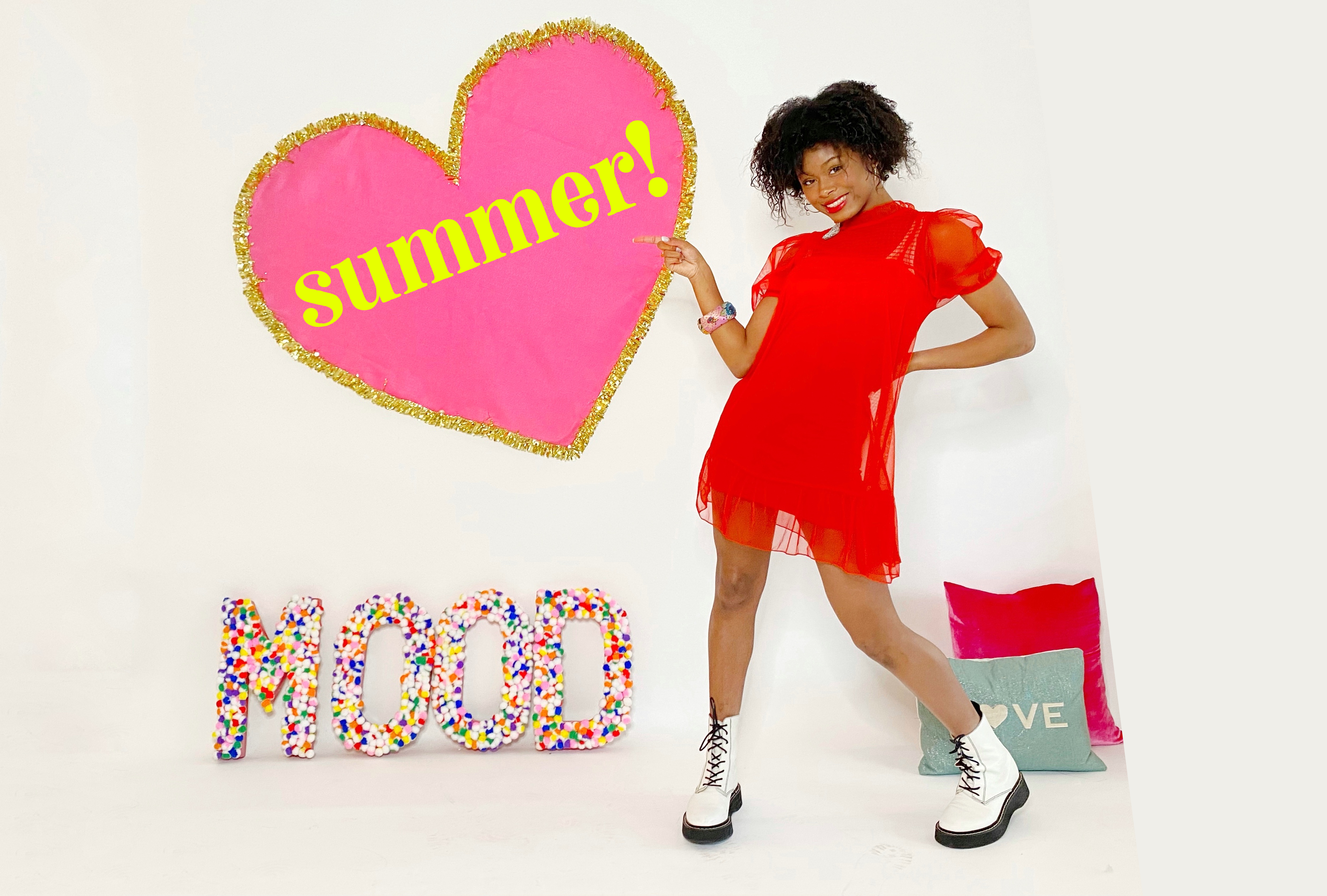 Dancer posing in red dress next to letters that spell out MOOD and pointing to a heart on the wall with the word summer inside it.